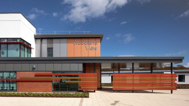 Front view of a modern style Woodland View mental healthcare building with decorative red and brown wood panels before a welcome sign at the entrance