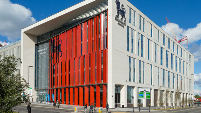 Corner view of a modern style red and white multistory university facade featuring a lion emblem in the school logo