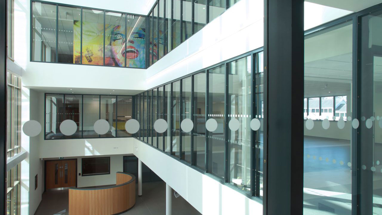 Interior view of a modern building atrium featuring glass walls, colorful artwork, and circular design elements.