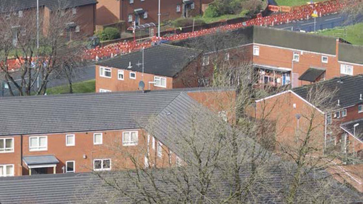 Aerial view of a residential area featuring brick houses with sloped roofs and surrounding greenery.