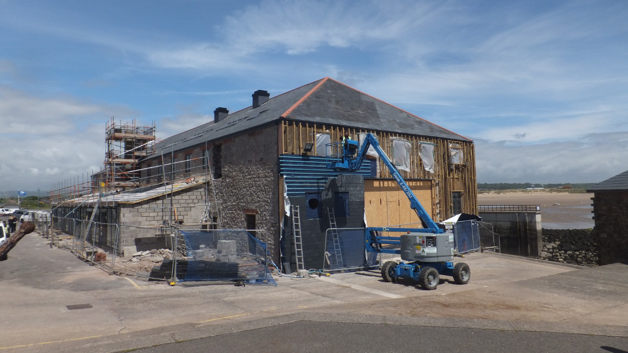 A large stone building under renovation with scaffolding, construction equipment, and a blue sky in the background.