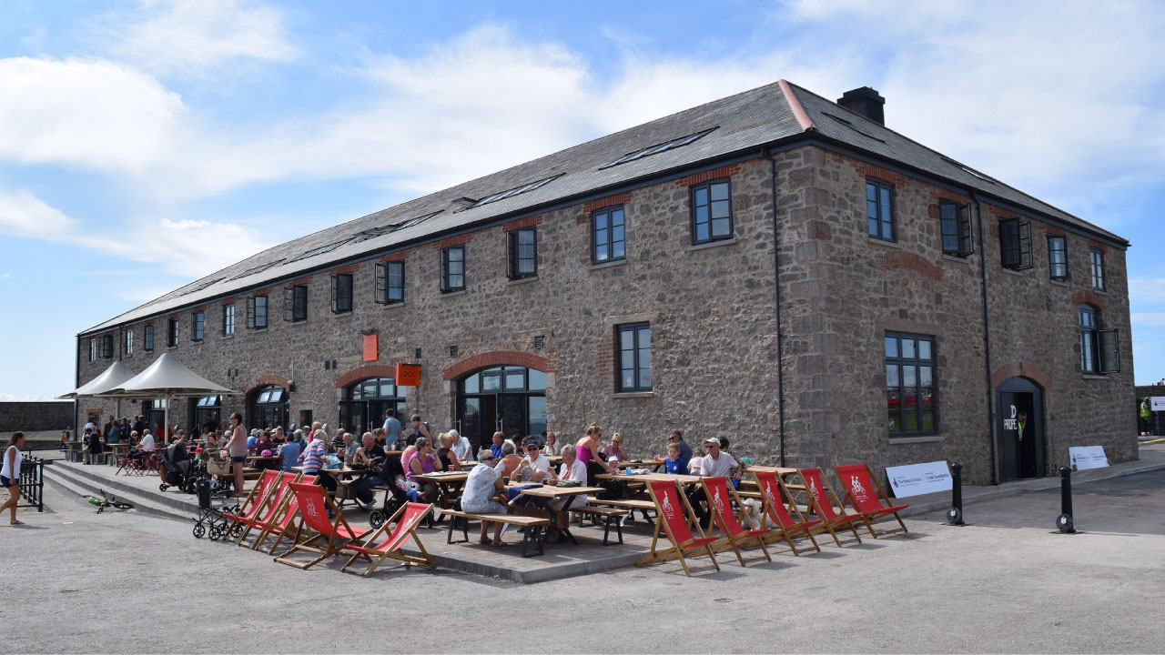 A lively outdoor dining area in front of a historic stone building, with people enjoying meals at picnic tables.