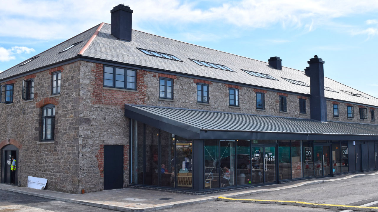 A renovated stone building with a modern glass entrance, featuring a café and a pizza place.