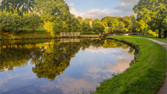 Curving garden path by water, reflecting clouds and trees