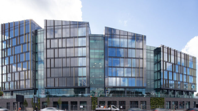 A large glass educational building with a bright blue sky behind it