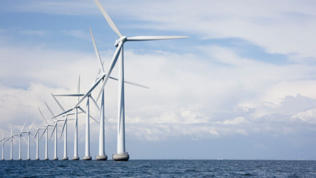 A line of wind turbines on the water and a cloudy but bright blue sky