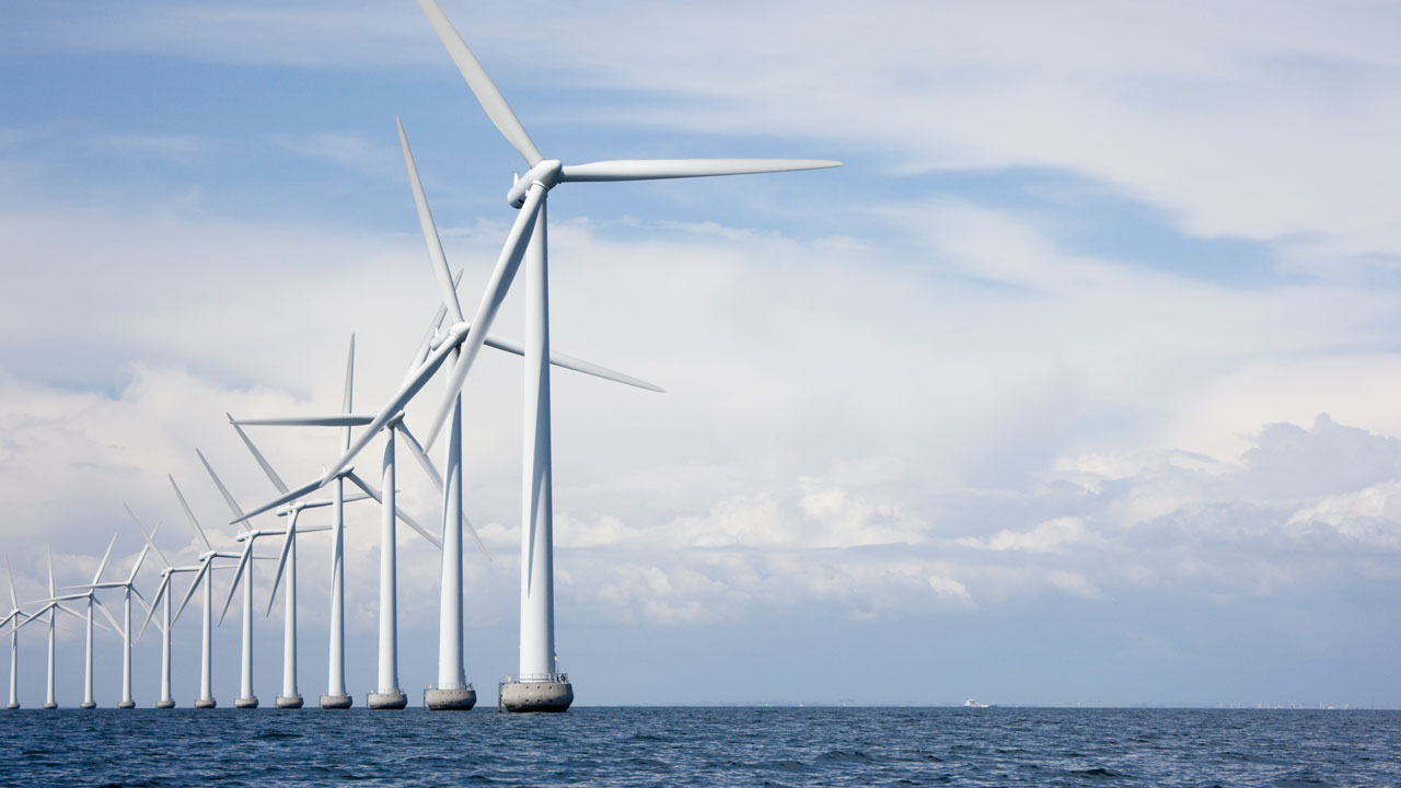 A line of wind turbines on the water and a cloudy but bright blue sky