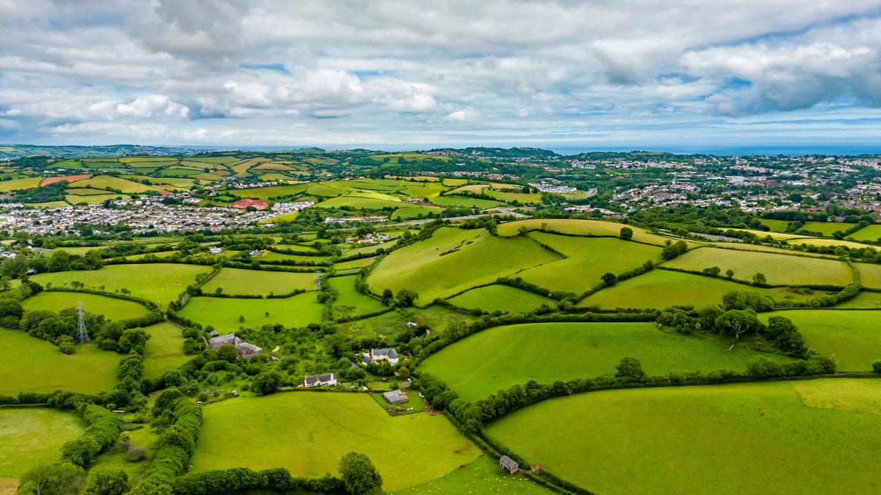 A green countryside comprising of fields with scattered housing in the distance