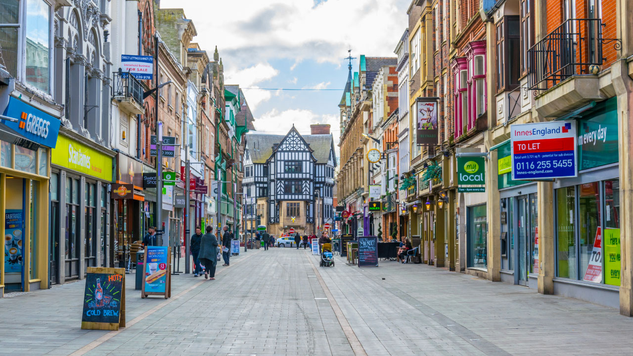 A bustling shopping street with a mix of modern shops and historic architecture, featuring a half-timbered building in the center.