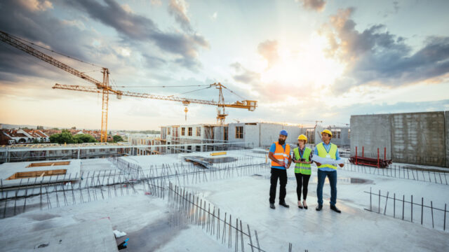 Three workers wearing PPE while standing on a commercial building roof