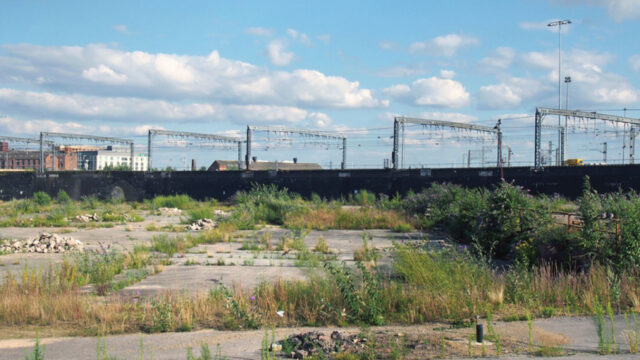An empty concrete pad with grass growing through the cracks, and power poles in the distance