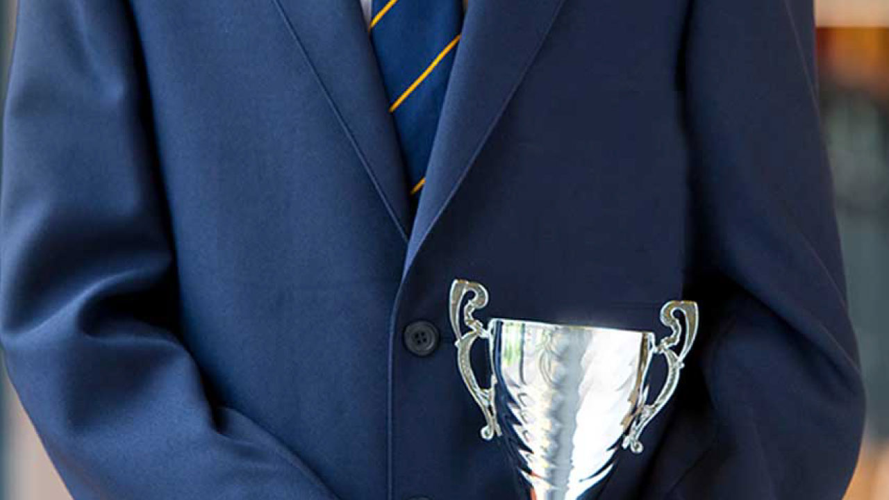 The arms of a child in navy blue school uniform holding a silver trophy