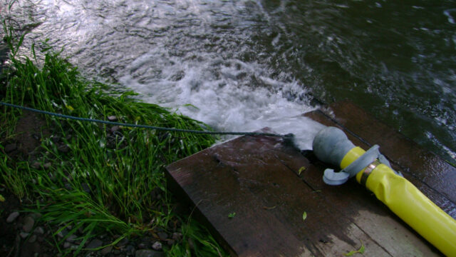 A large water hose sitting on a wooden structure and spraying water into a steam