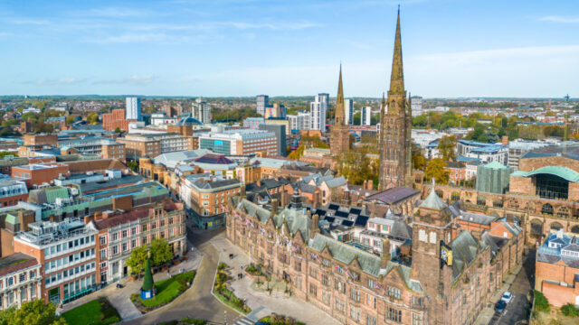 Aerial view of a cityscape featuring historic and modern buildings, including two prominent church spires, with a mix of greenery and urban architecture.