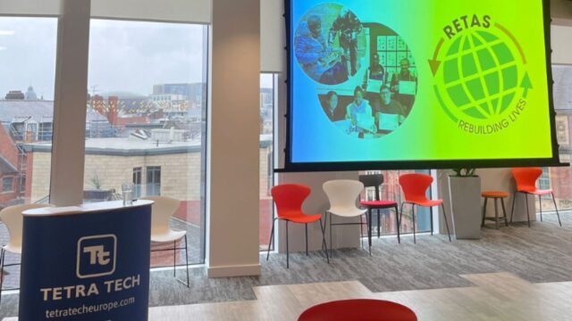 An office space with a Tetra Tech podium and a screen displaying the RETAS charity organisation logo.