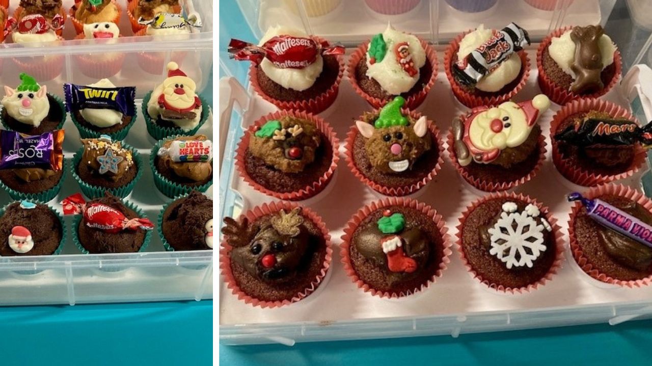 Two plastic containers filled with decorated Christmas-themed cupcakes. The cupcakes are topped with festive decorations like Santa faces, reindeer, snowflakes, elves, candy pieces, and holiday-themed icing.