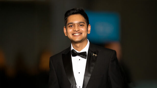 Young man in a black tuxedo smiling at a formal event.