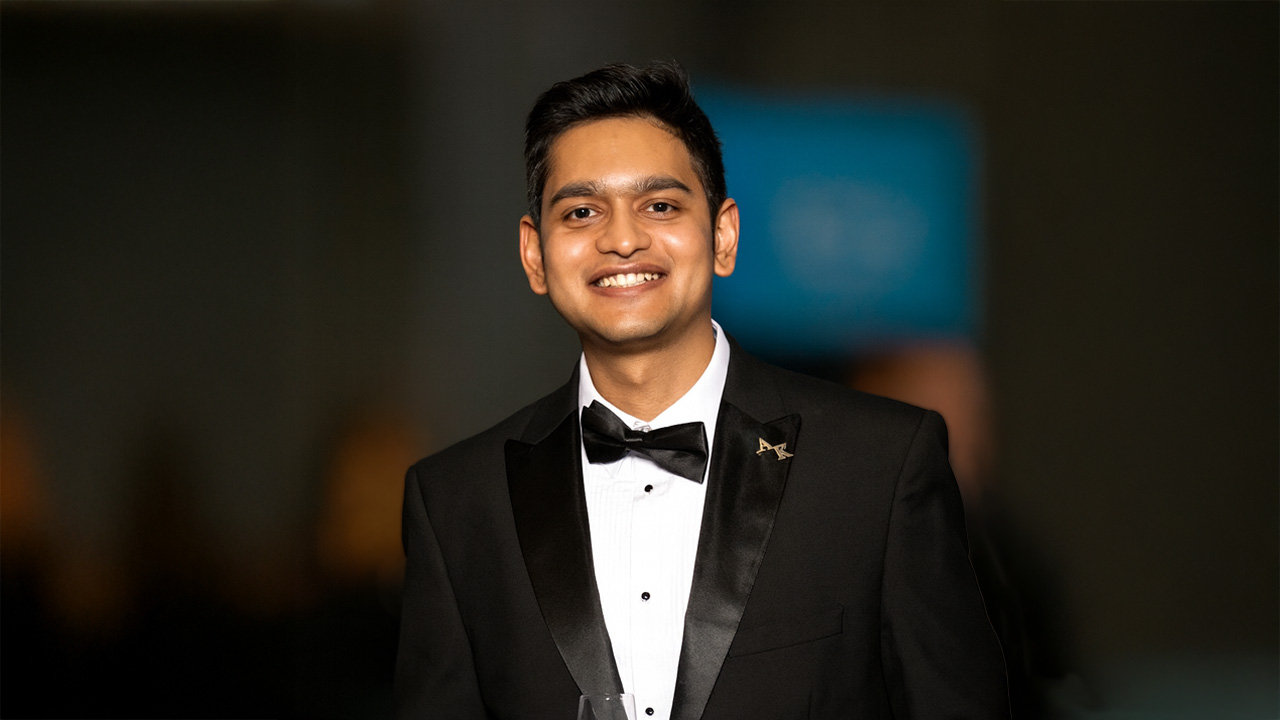 Young man in a black tuxedo smiling at a formal event.